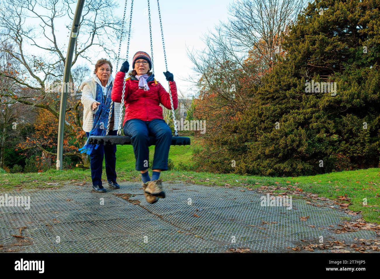 3 giocose donne anziane oltre i 60 anni si rilassano giocando a swing nel parco il giorno autunnale a Hermitage Park, Helensburgh, Argyll e Bute, Scozia Foto Stock