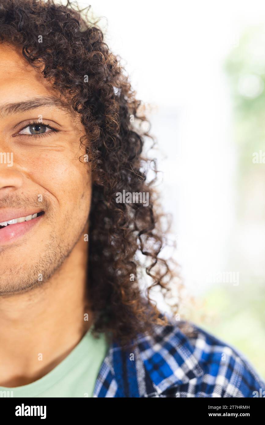 Mezzo volto di felice uomo birazziale con lunghi capelli ricci scuri sorridenti nel soleggiato soggiorno, spazio fotocopie Foto Stock