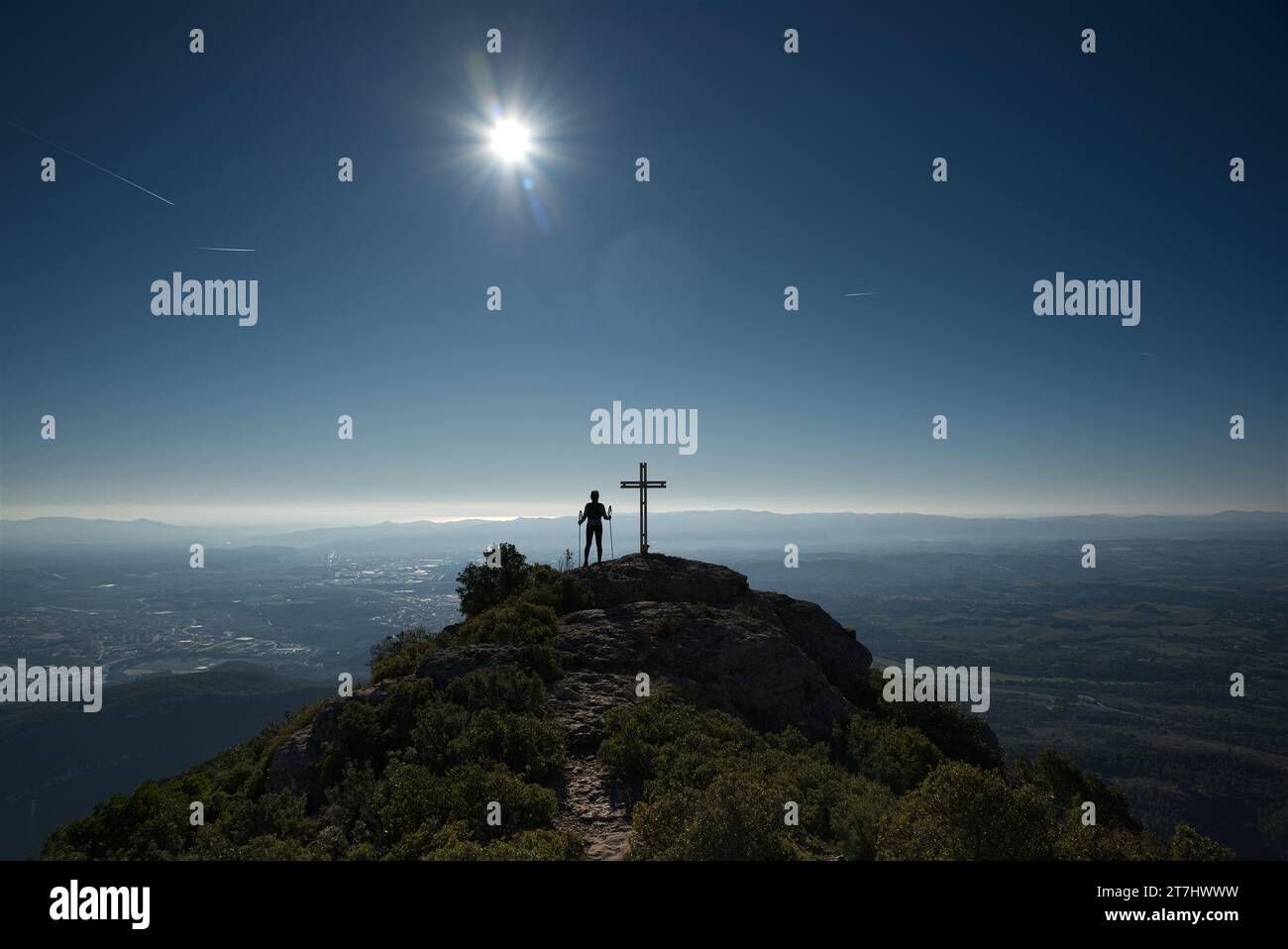 La donna contempla l'imponente paesaggio accanto a una croce dalla cima di una montagna. Foto Stock