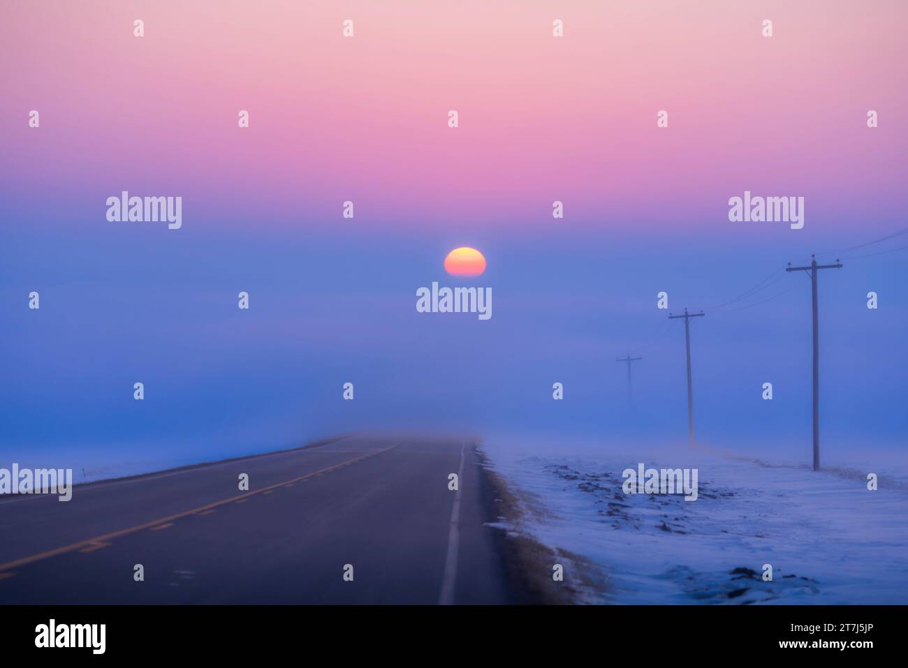 Il tramonto del sole che scende in un banco nebbia su un'autostrada rurale che guarda verso ovest, la sera dell'equinozio di vernal, 20 marzo 2023. Quindi il Sole è se Foto Stock