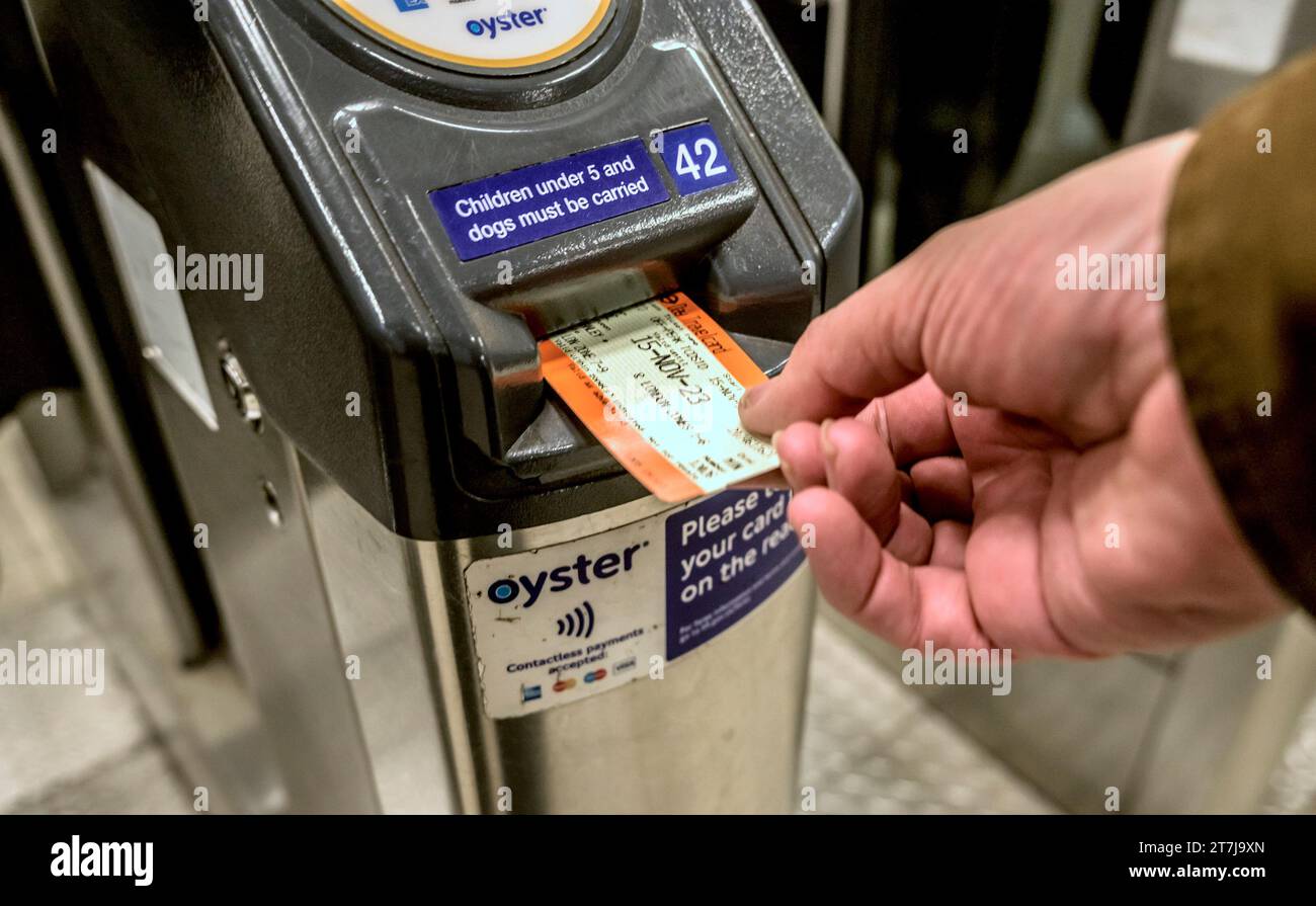 Londra, Regno Unito. Il passeggero della metropolitana che mette un biglietto attraverso una biglietteria in una stazione della metropolitana Foto Stock