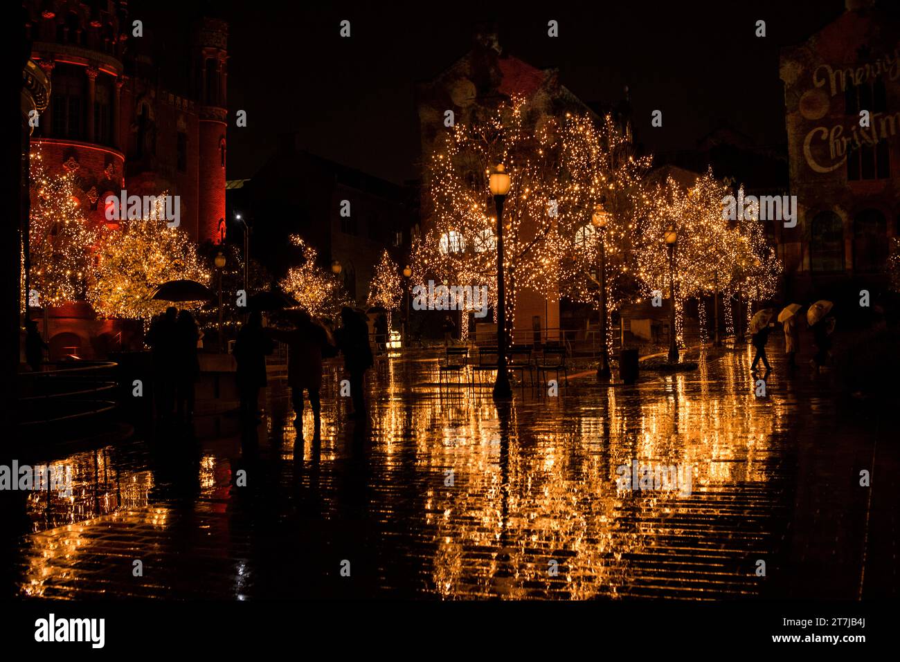 La magia delle feste si svolge mentre le luci natalizie baciate dalla pioggia adornano gli alberi, proiettando riflessi scintillanti sul terreno bagnato sotto l'incantevole velo di una vittoria Foto Stock