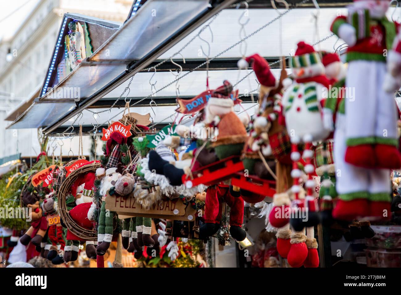 L'abbraccio natalizio del mercato di Santa Llucia: Una vivace bancarella piena di peluche natalizie, adornata da "Feliz Navidad" e "Bon Nadal", che cattura il Foto Stock