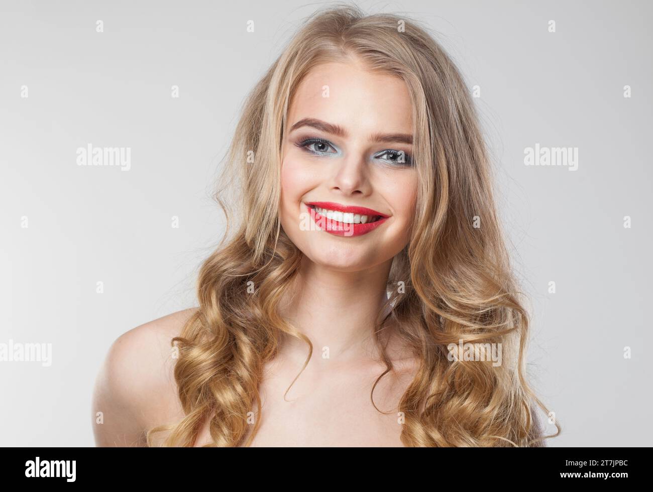 Amichevole positivo felice donna con trucco e capelli ondulati biondi lunghi e sani che posa su sfondo bianco parete studio. Bellezza emotiva della moda Foto Stock