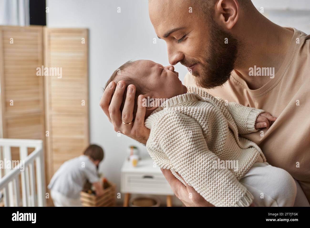 concentratevi sul padre che tiene amorevolmente il suo neonato con il figlio piccolo che gioca sullo sfondo, la famiglia Foto Stock
