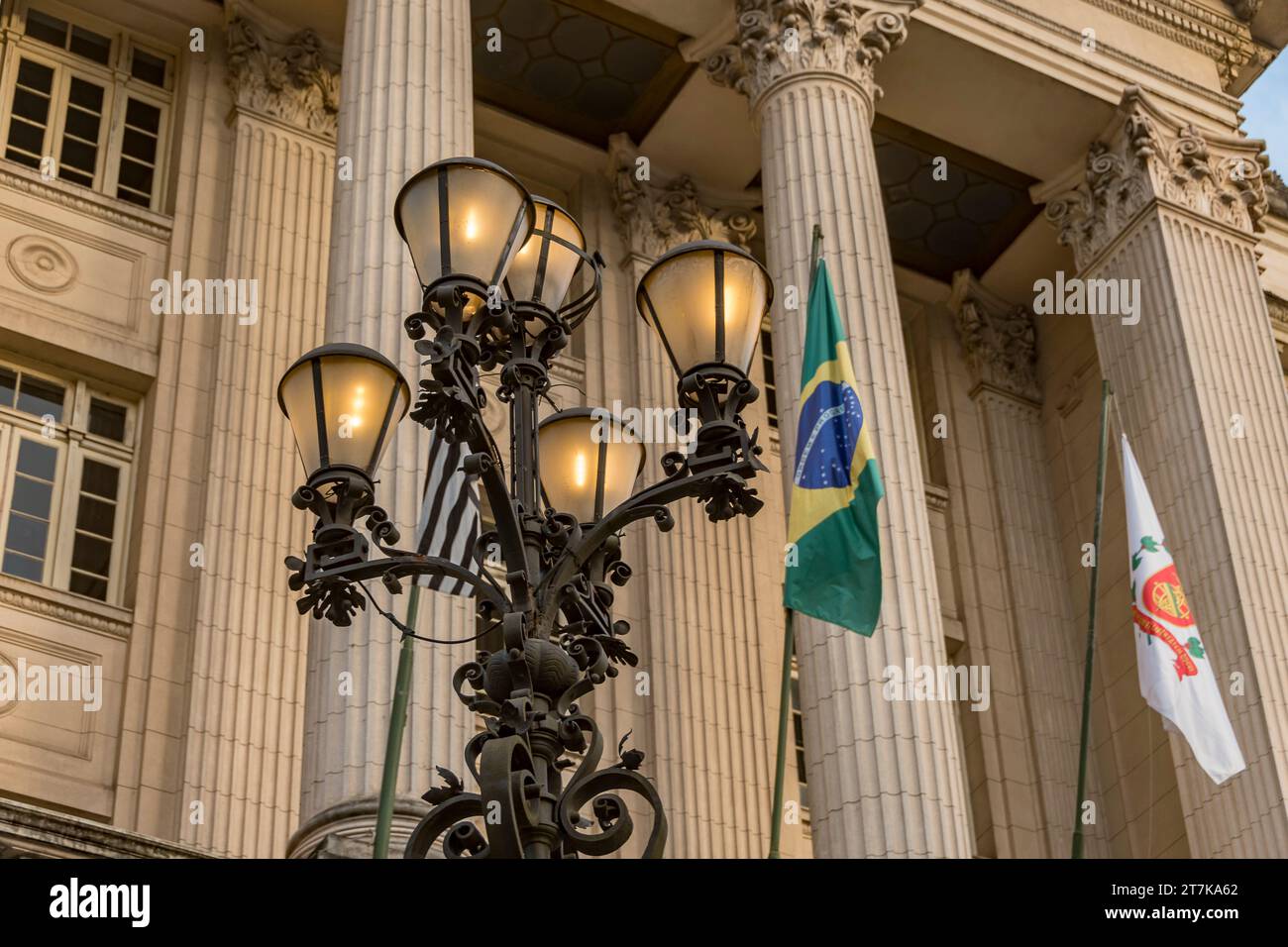 Vecchia lampada illuminata con la facciata dell'edificio del municipio di Santos sullo sfondo. Bandiere dello Stato di São Paolo, del Brasile e della città di Santos. Foto Stock