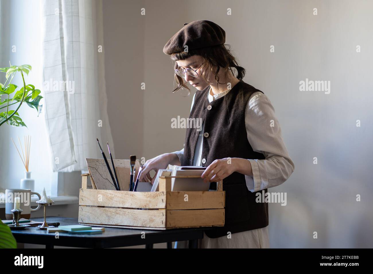 Animatore pensivo freelance con scatola in legno contenente accessori per la pittura per la preparazione del luogo di lavoro Foto Stock
