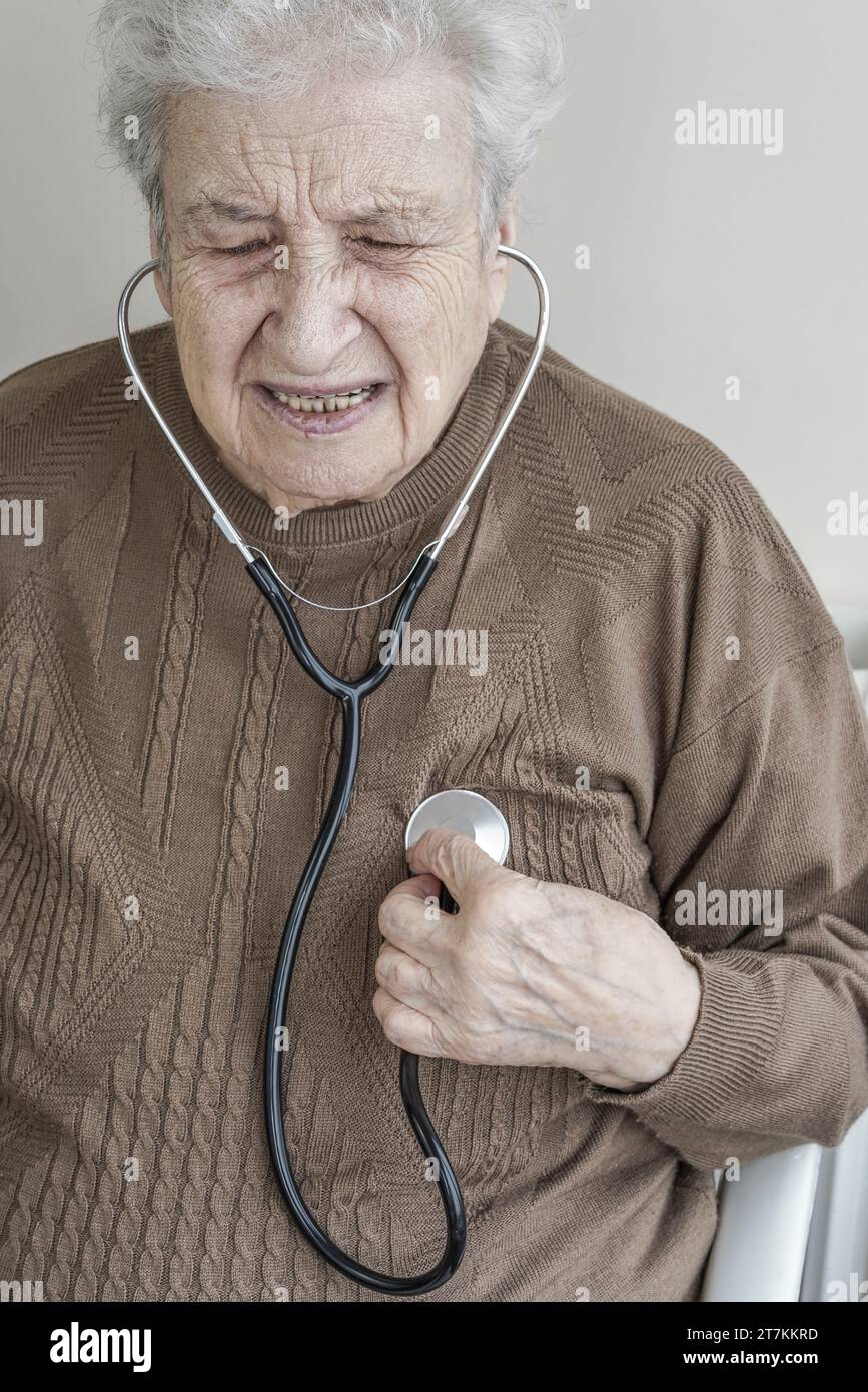 Una donna anziana che ascolta il suo cuore con lo stetoscopio Foto Stock