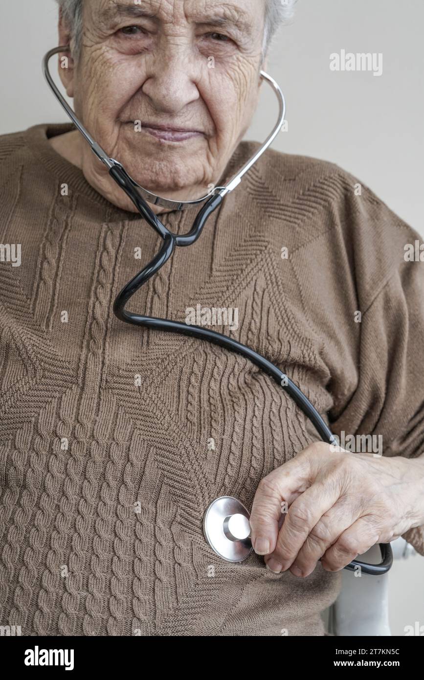 Una donna anziana che tiene uno stetoscopio per ascoltare il suo stomaco Foto Stock