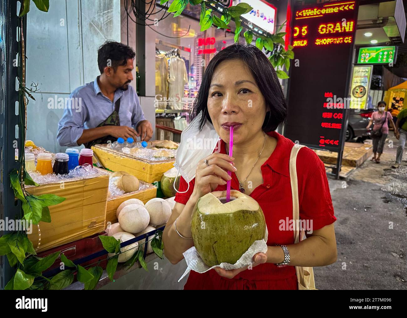 Una donna vietnamita beve una noce di cocco fresco verde acquistato da un venditore per le strade di Bangkok in Thailandia. Foto Stock