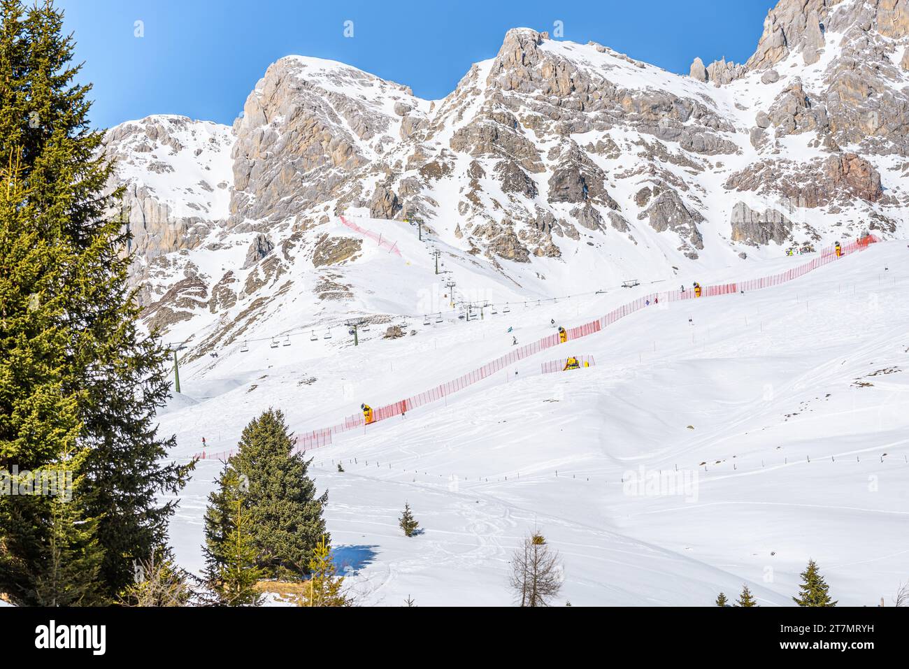 Seggiovie e piste da sci ai piedi delle cime rocciose innevate delle Alpi in una soleggiata giornata invernale Foto Stock
