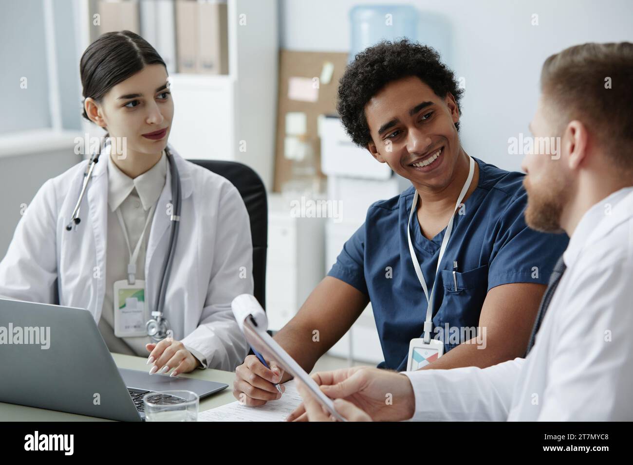 Gruppo multietnico di giovani medici sorridenti che lavorano insieme alla scrivania in clinica Foto Stock