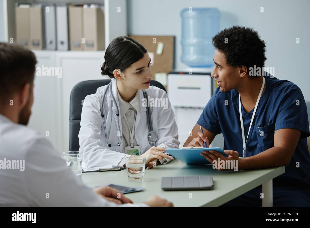 Ritratto laterale di due giovani medici che discutono di questioni di lavoro durante una riunione presso l'ufficio della clinica Foto Stock
