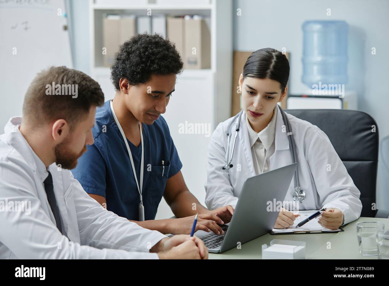 Gruppo multietnico di tre giovani medici che guardano lo schermo del notebook mentre lavorano insieme durante una riunione Foto Stock