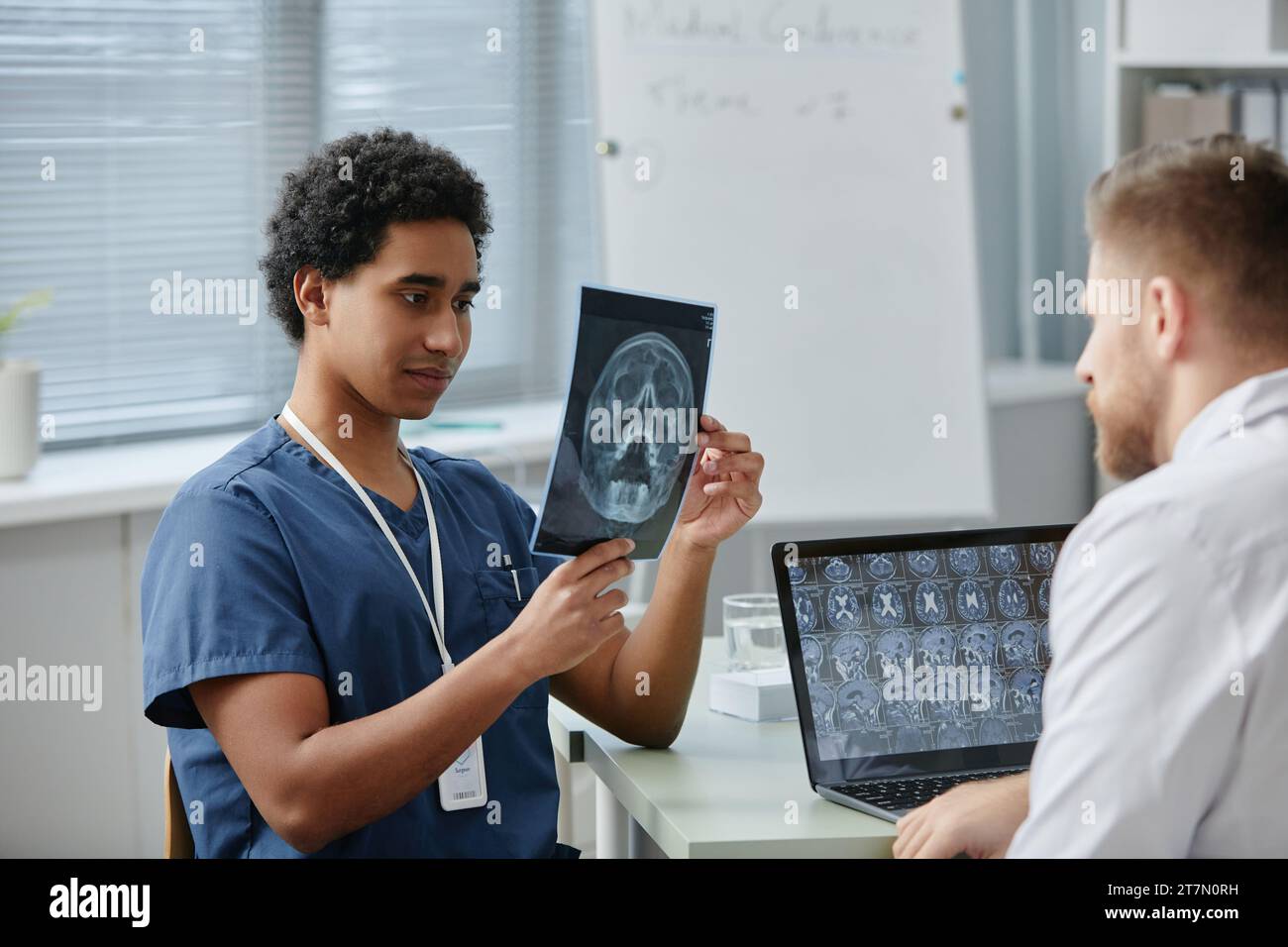 Ritratto di un giovane medico che tiene l'immagine a raggi X del cervello mentre discute del caffè dei pazienti con un collega in clinica Foto Stock