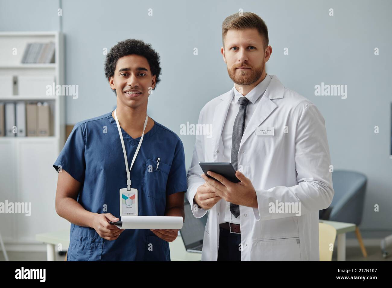Ritratto in vita di due medici maschi sorridenti davanti alla macchina fotografica in piedi nell'ufficio della clinica Foto Stock