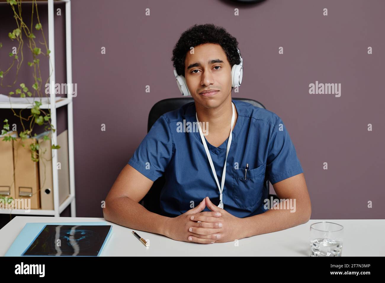 Ritratto frontale di un giovane arabo come medico seduto sul posto di lavoro in clinica e ascoltando musica con le cuffie e lo spazio fotocopie Foto Stock
