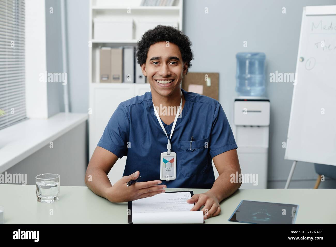 Ritratto di un giovane uomo del Medio Oriente sorridente come medico che parla tramite video chat in clinica, spazio copia Foto Stock