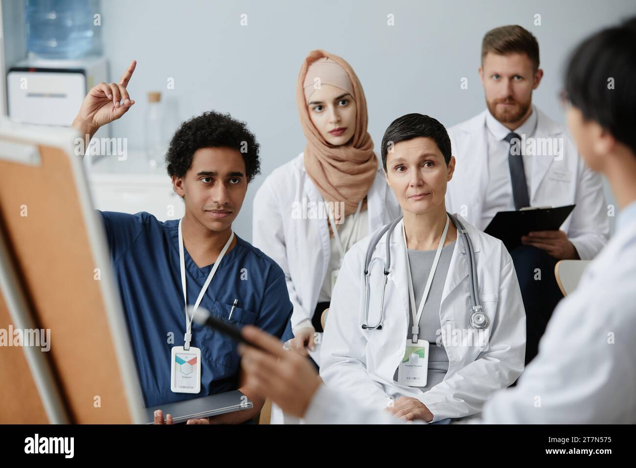 Ritratto di giovane uomo mediorientale alzando la mano in pubblico al seminario medico Foto Stock