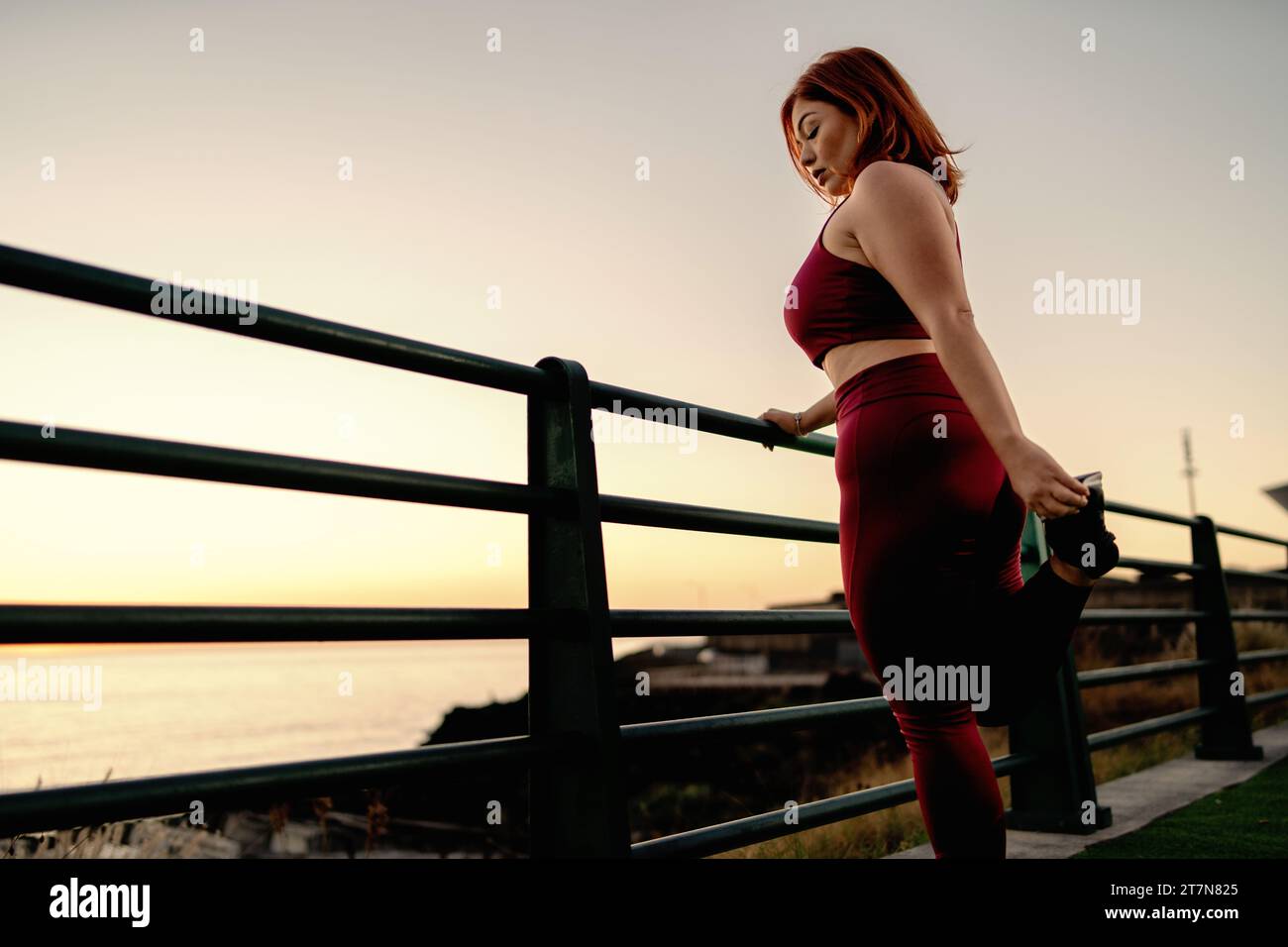 Donna Plus-size che si allunga con gioia durante una sessione di yoga al tramonto, celebrando la salute e la positività del corpo. Foto Stock