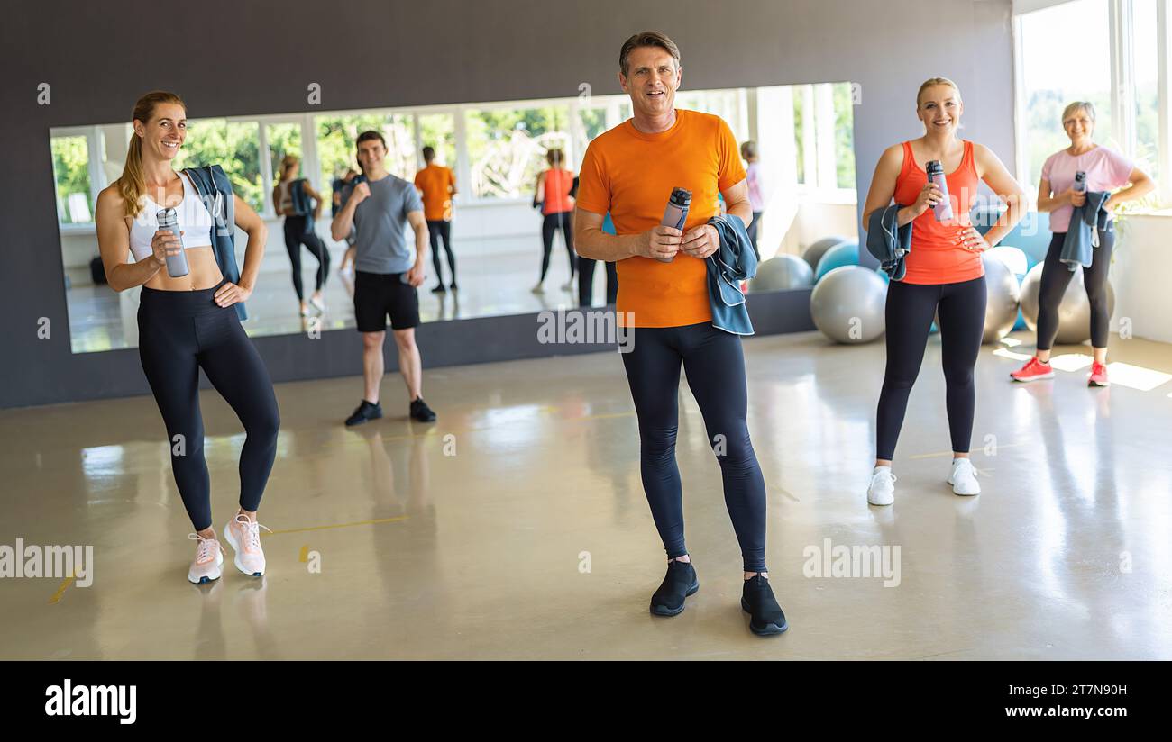 Persone con attrezzature da palestra sorridenti in un centro fitness, palle da ginnastica sullo sfondo. Immagine del concetto di lavoro di squadra Foto Stock