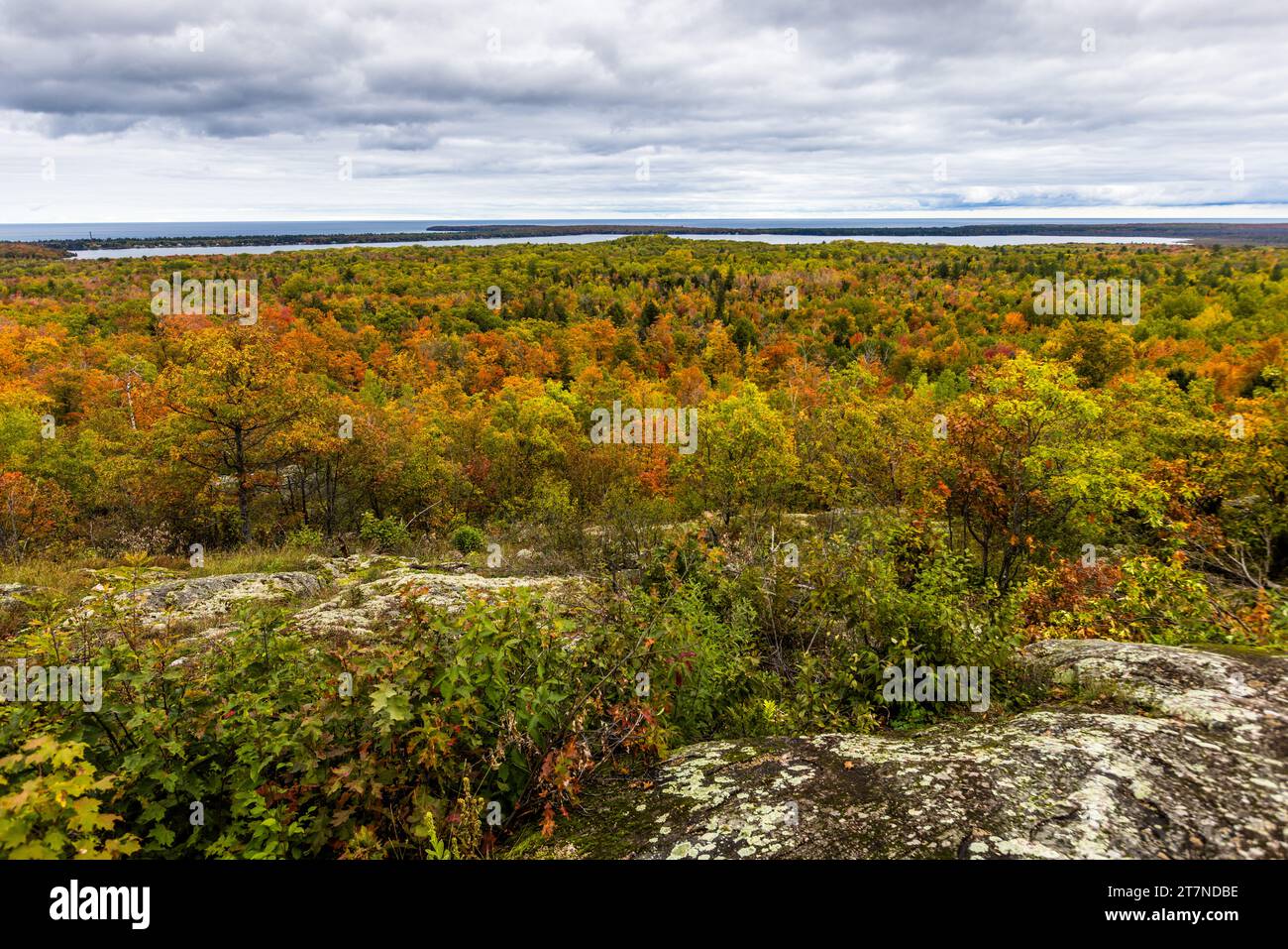Il punto panoramico del Sugarloaf Mountain sulla Big Bay Road nel Powell Township, Michigan, Stati Uniti, offre, con un clima autunnale da "Indian summer", una vista panoramica su una foresta dai colori vivaci fino al Lago Superiore. Rocce ricoperte di licheni costeggiano lo sfondo della veduta. Foto Stock