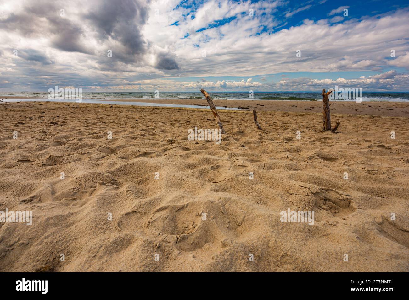 Splendido paesaggio di mare tempestoso visto da una grande spiaggia sabbiosa piena di dune e con tre grandi picchetti portati a terra Foto Stock