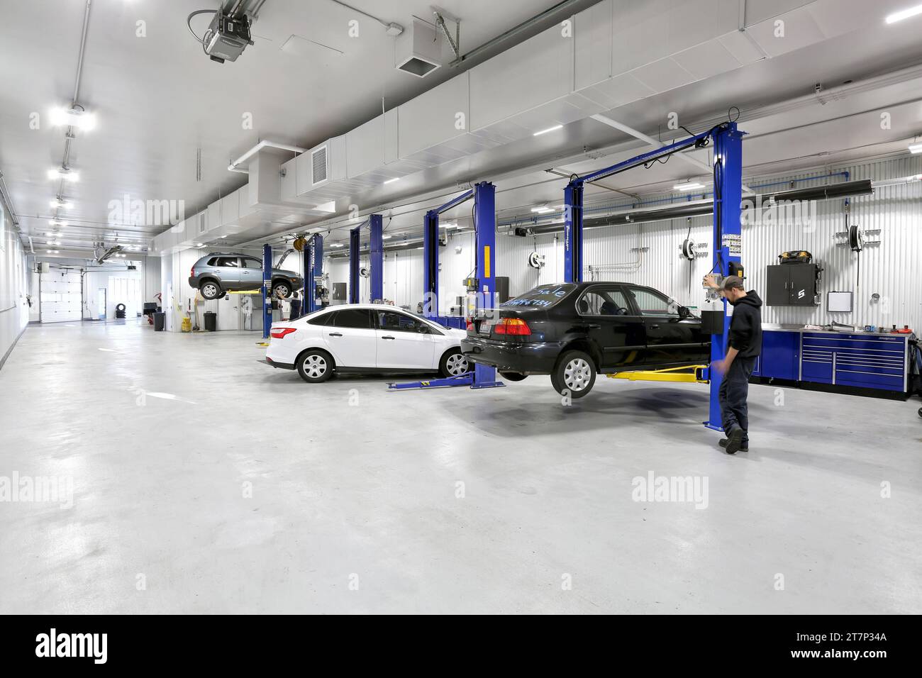 Un meccanico che solleva un'auto su un sollevatore idraulico in un'officina di riparazione auto nuova e moderna. Foto Stock