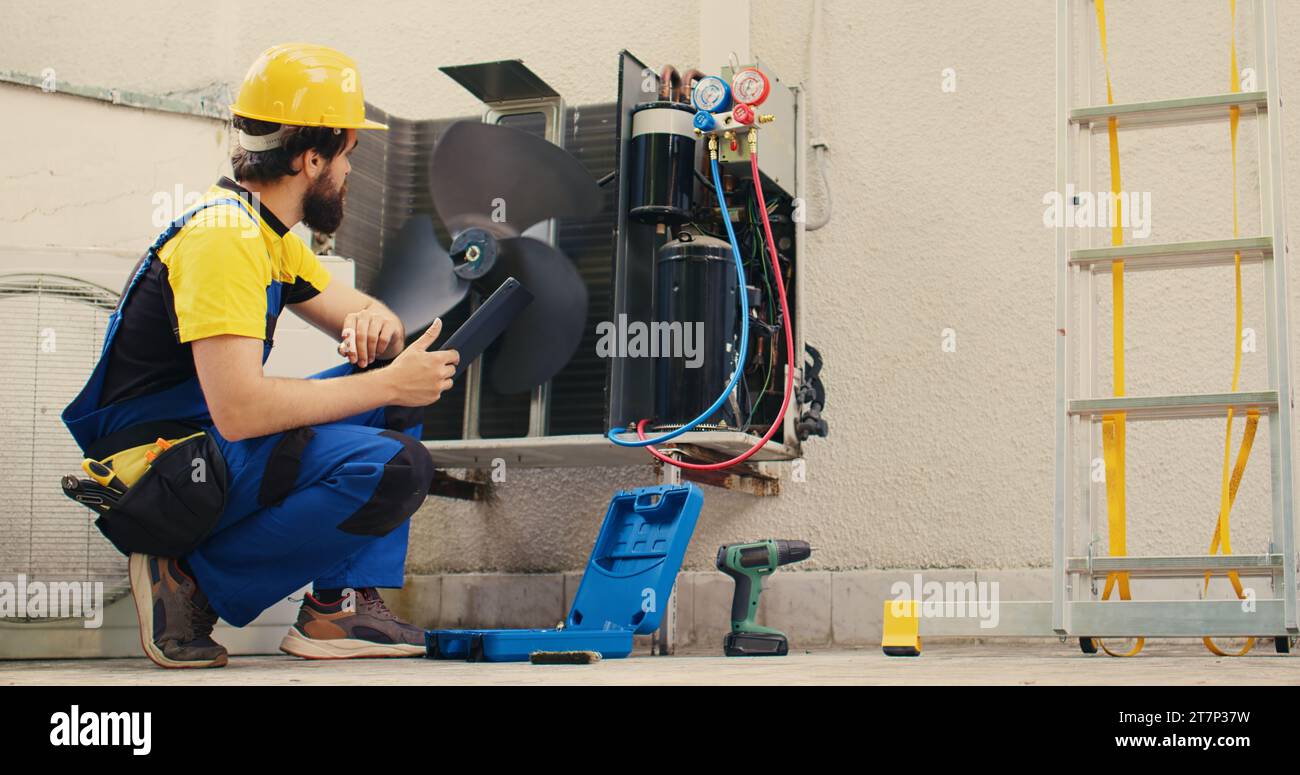 Un tecnico qualificato incaricato della manutenzione ordinaria del sistema hvac esterno, alla ricerca di problemi relativi al refrigerante. Tecnico qualificato che esegue l'ispezione del condizionatore d'aria, scrivendo i dati sul tablet Foto Stock