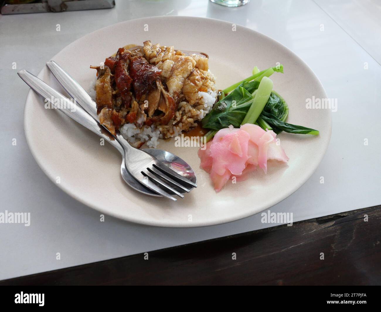 Anatra arrosto e maiale croccante su riso con bok choy bollito e zenzero sottaceto rosa su un piatto bianco, cibo fusion cinese in Thailandia Foto Stock