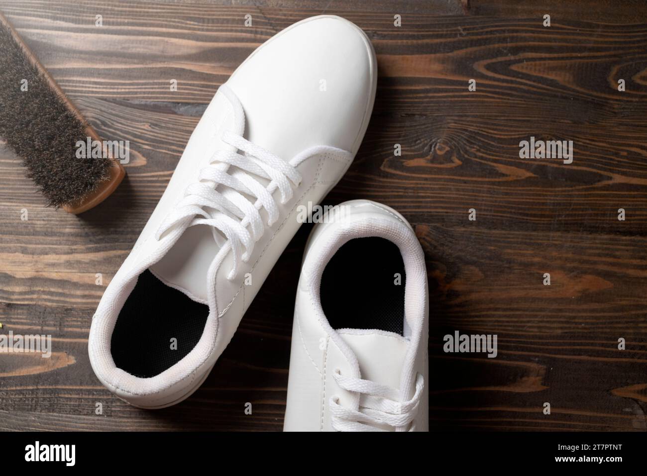 Spazzola con sneaker bianche su uno sfondo di legno. Concetto di cura delle scarpe Foto Stock