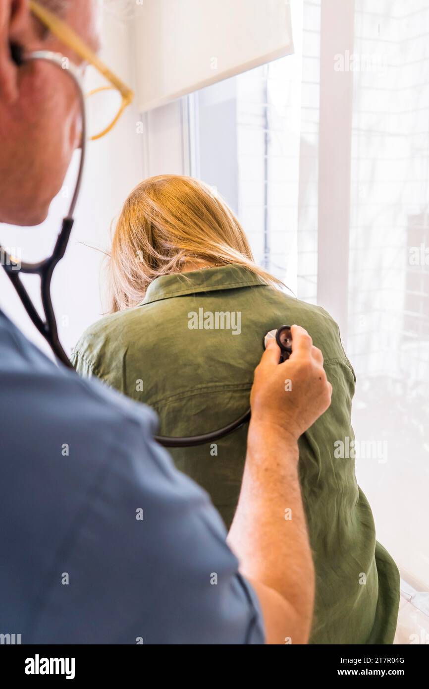 Medico che usa stetoscopio sulla schiena del paziente per ascoltare i polmoni per problemi respiratori. Scatto verticale Foto Stock