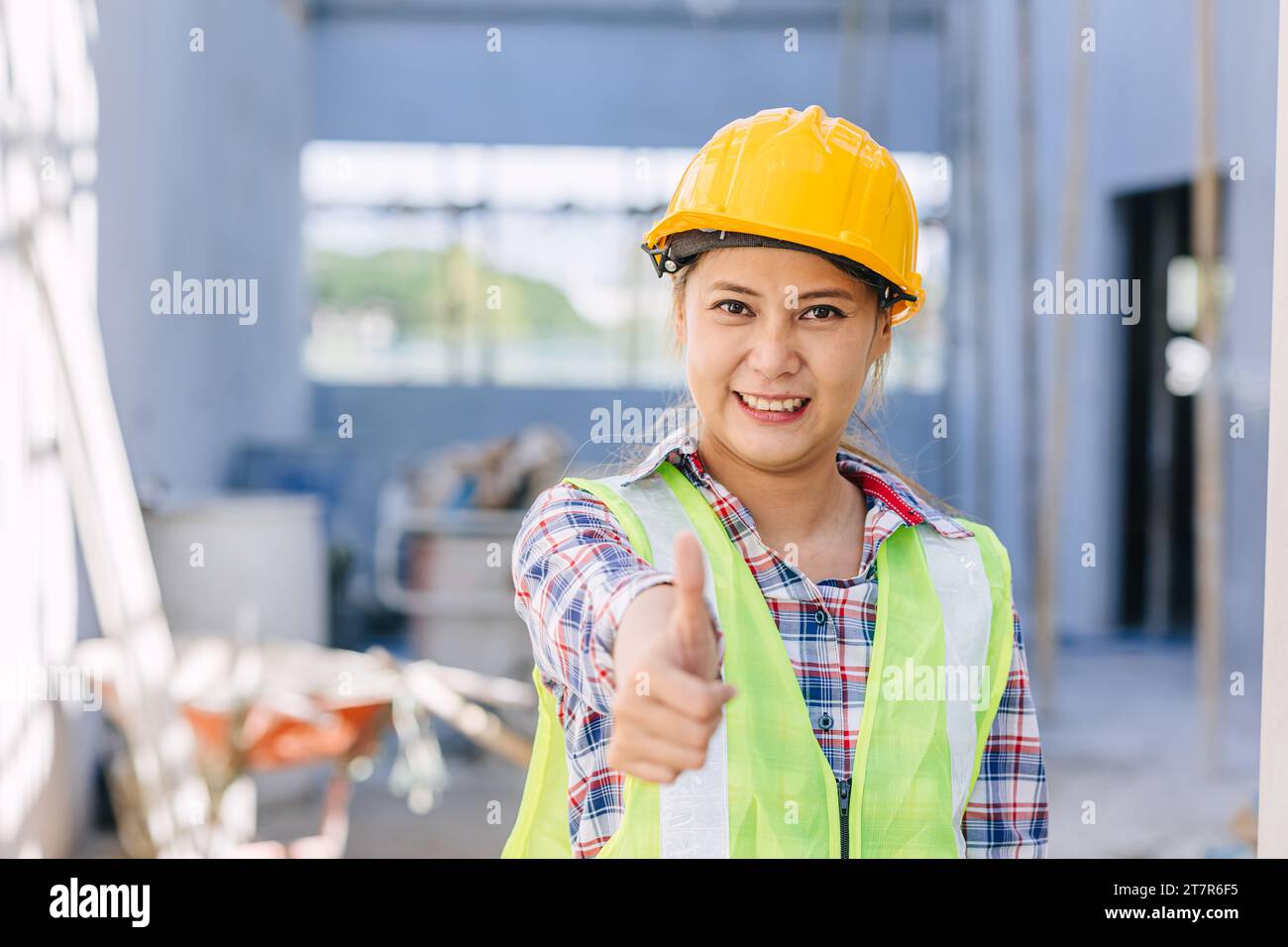 Donna asiatica operaia edile felice sorridente pollice sullo sfondo del cantiere edile Foto Stock