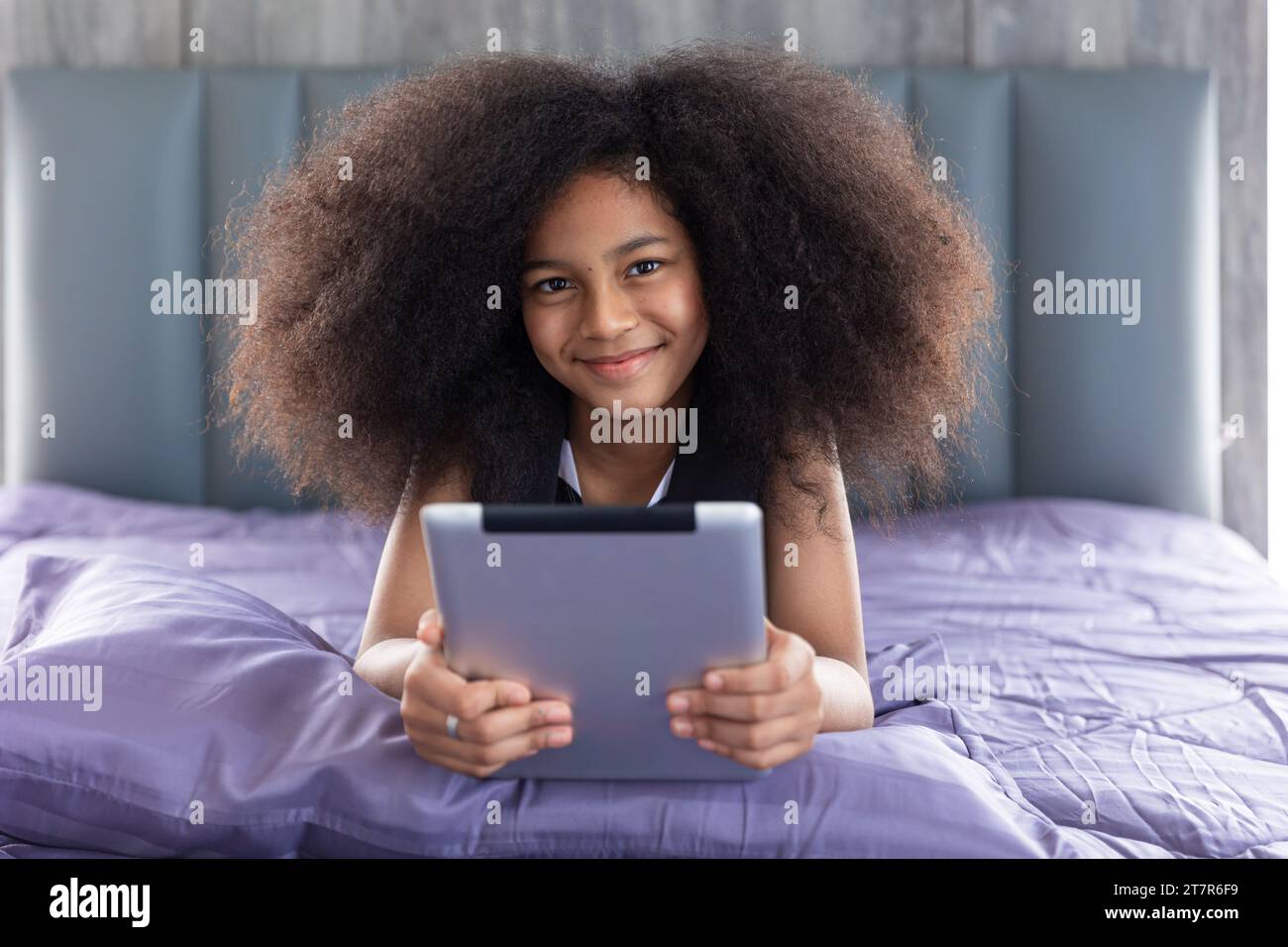 Bambina nera africana capelli afro adorabili sdraiati sul letto con un tablet e un buon autoapprendimento durante le vacanze a casa, una macchina fotografica che sorride un ritratto. Foto Stock