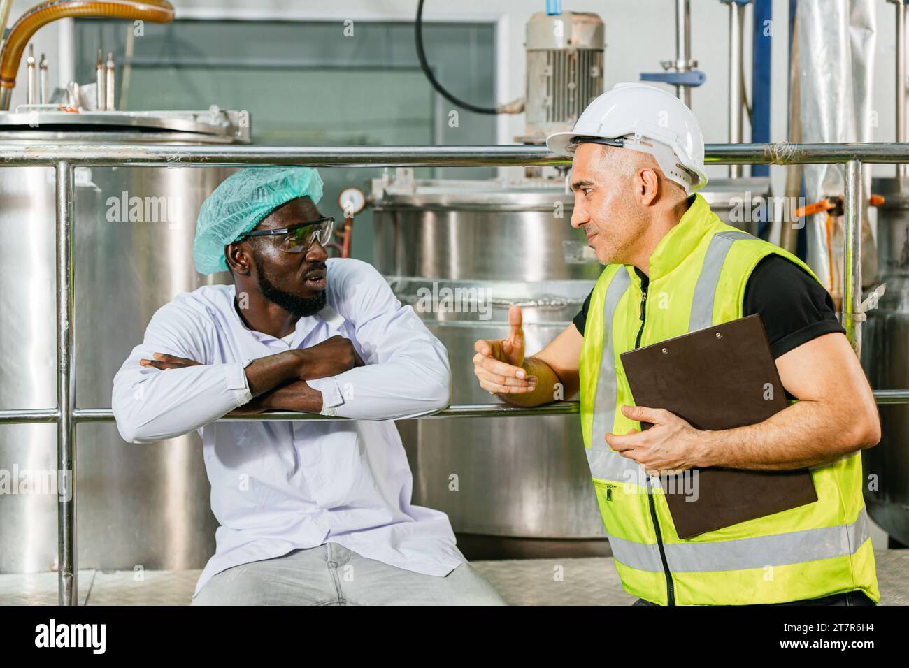 Ingegnere responsabile della sicurezza lavoratore che parla con un amico lavoratore della linea di produzione nella fabbrica di alimenti e bevande Foto Stock