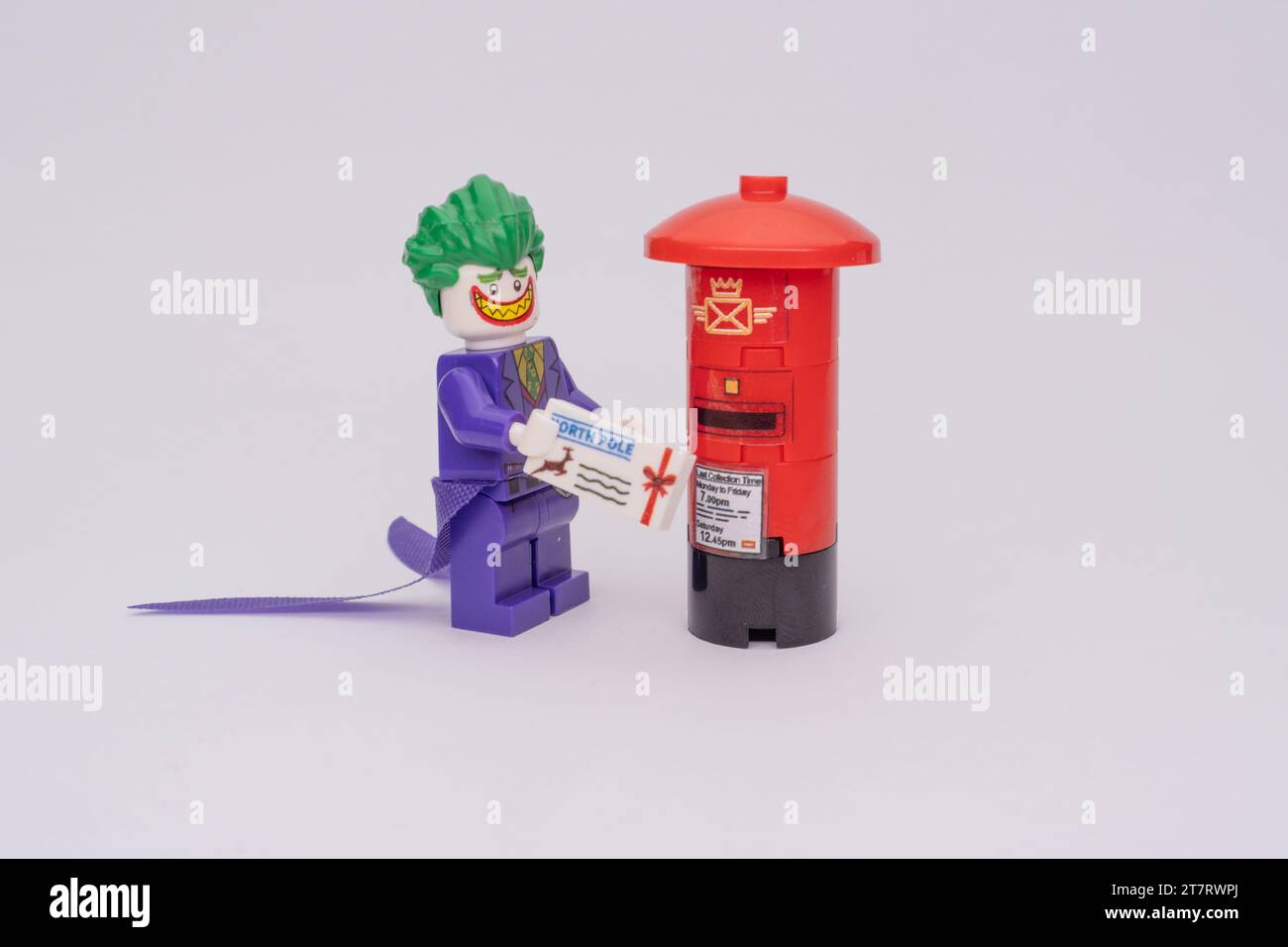 Una minifigura LEGO di Joker in piedi vicino a una cabina telefonica rossa, che tiene la posta in mano. Foto Stock