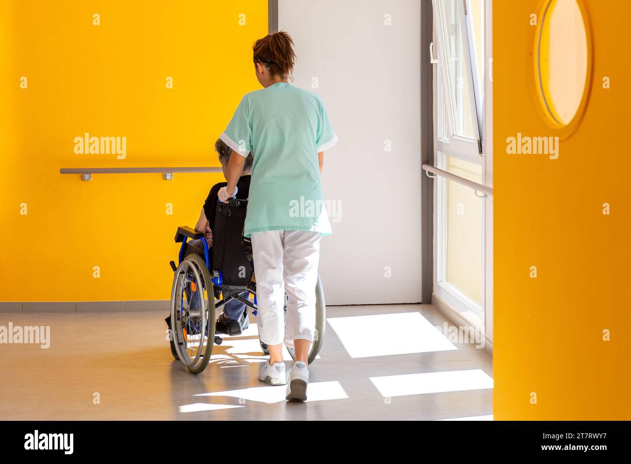 Un assistente accompagna una persona anziana sulla sedia a rotelle nella casa di cura Foto Stock