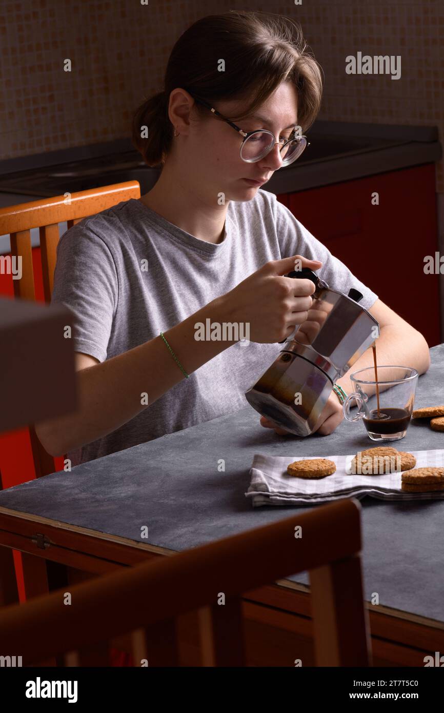 Giovane donna che versa il caffè della moka nella tazza in cucina Foto Stock