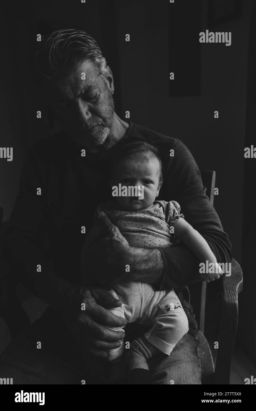 Il neonato è tenuto dal nonno, sia serio, bianco e nero Foto Stock