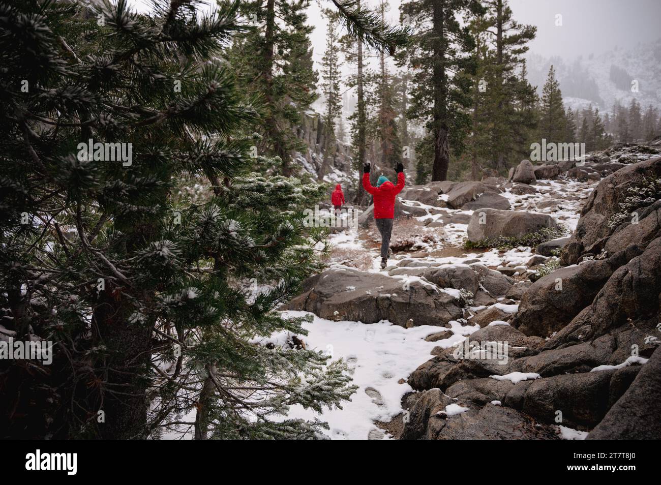 I bambini in camici rossi saltano con gioia lungo un sentiero nella neve Foto Stock