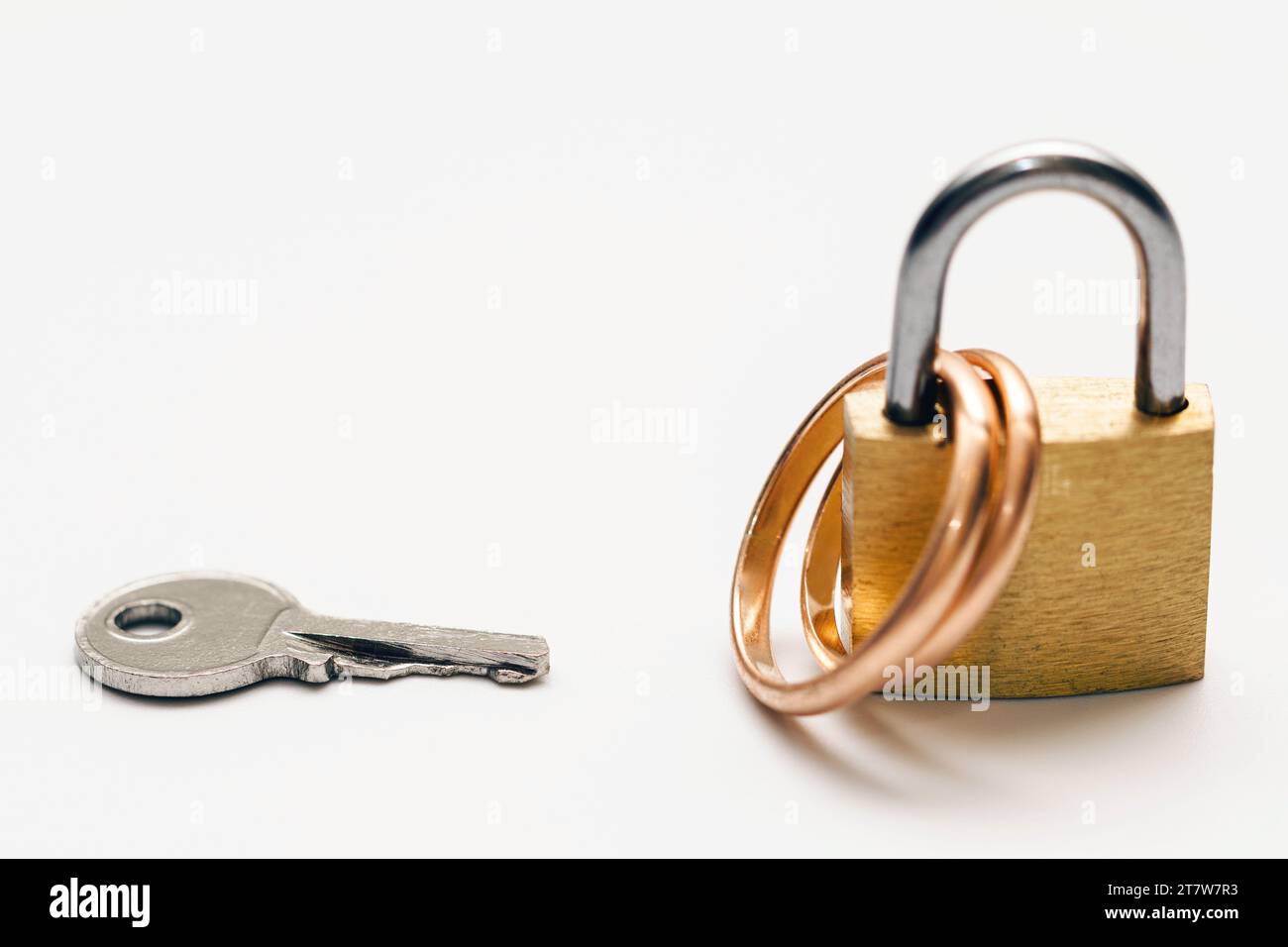 Una piccola chiave e due fedi nuziali dorati chiusi su un lucchetto Foto Stock