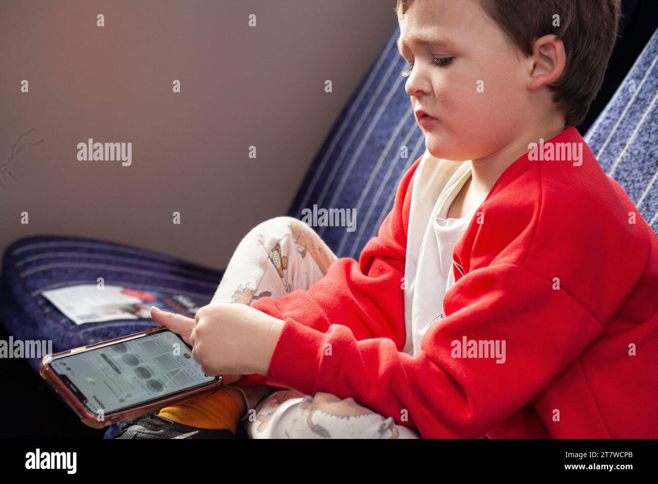 Tech-Savvy Journey: Un bambino di 6 anni impegnato nei giochi per smartphone durante un viaggio in treno, il suo volto angelico pieno di concentrazione. Foto Stock