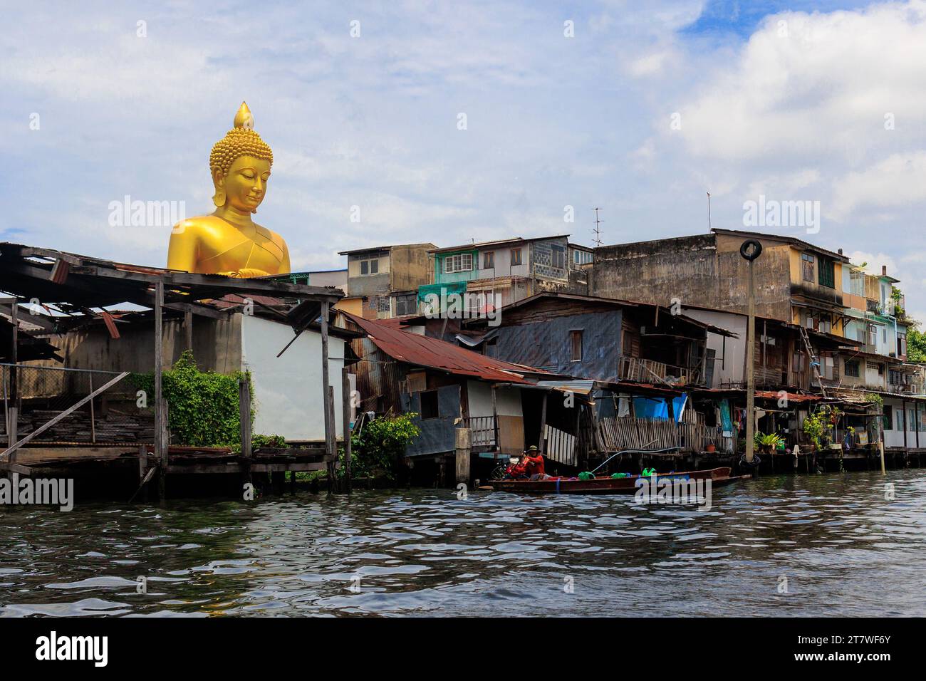 La statua gigante del Buddha Dhammakaya Thep Mongkol che si fonde dalle vecchie case di legno di Bangkok Foto Stock