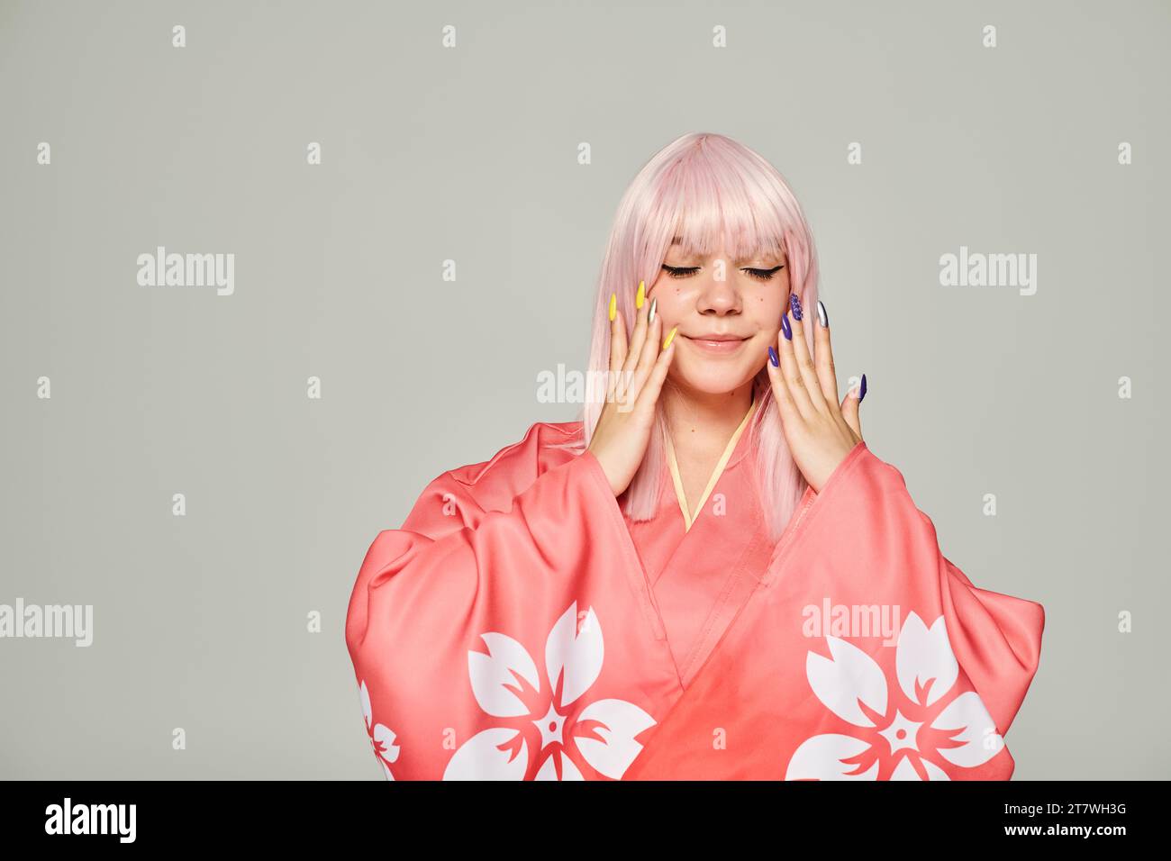 donna in stile anime in kimono rosa con stampa floreale e mani con manicure colorata su sfondo grigio Foto Stock