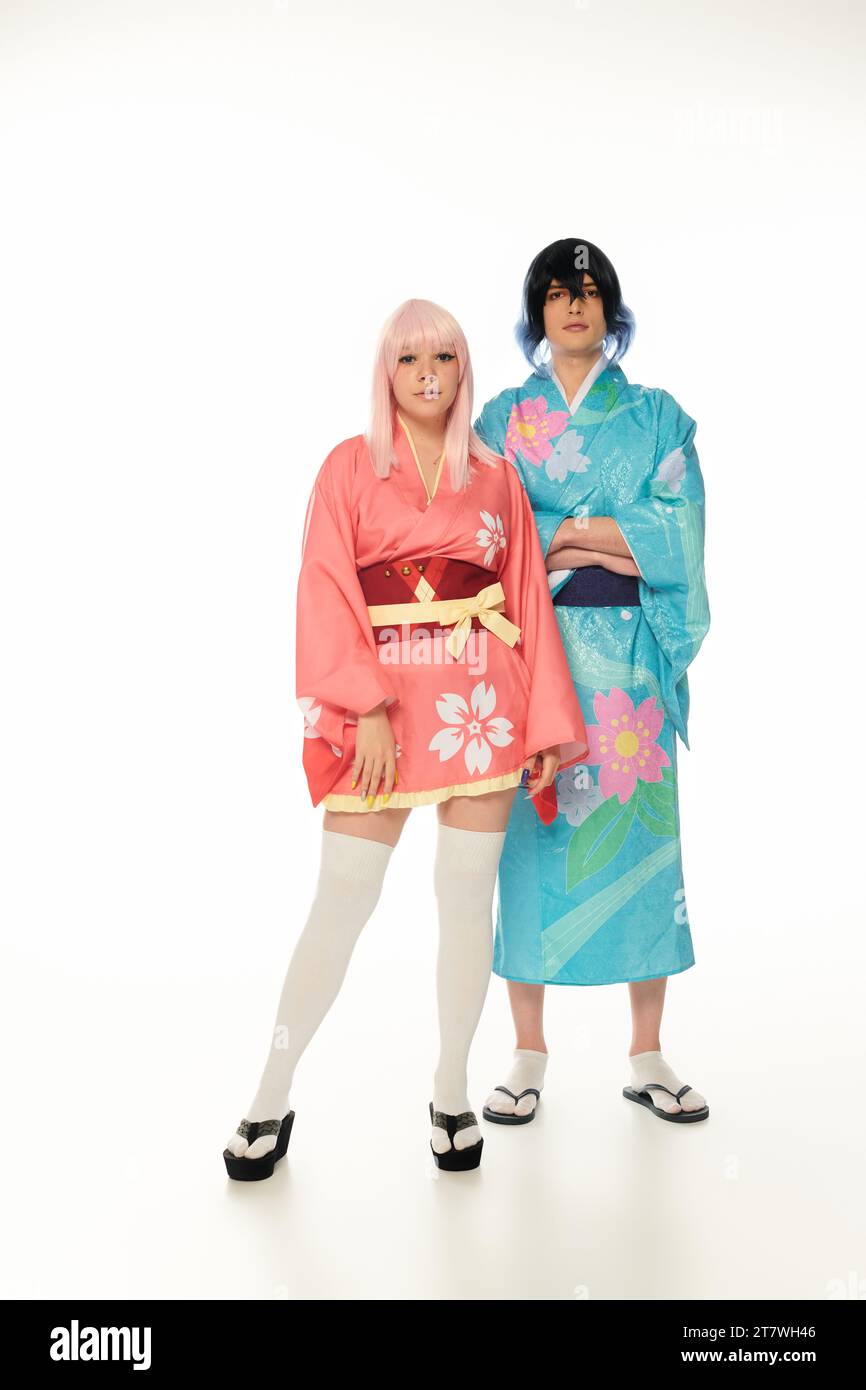 coppia in stile anime con un vivace abbigliamento tradizionale e parrucche che guardano la fotocamera su bianco, a tutta lunghezza Foto Stock
