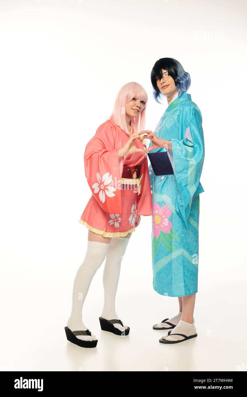 allegri giovani cosplayer in kimono colorati che mostrano il segno del cuore con le mani su uno stile anime bianco Foto Stock