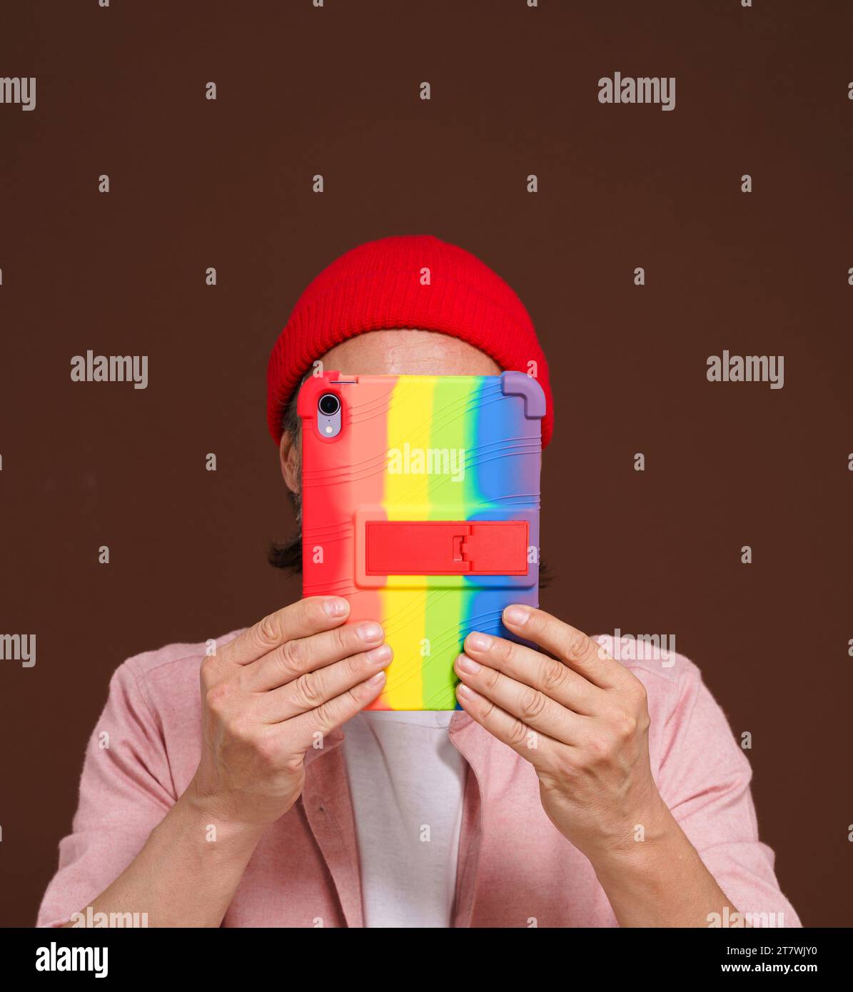 Una persona anonima nasconde il volto su un tablet PC con colori arcobaleno gay LGBT. Intersezione tra identità digitale e orgoglio LGBTQ, sottolineando la necessità di privacy e protezione nello spazio digitale del movimento gay Pride. Foto di alta qualità Foto Stock