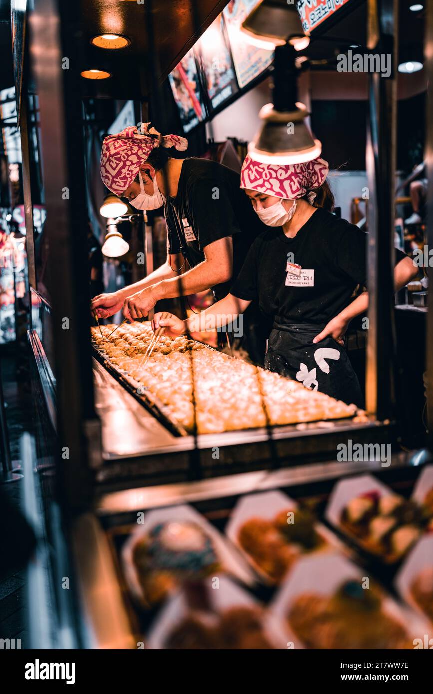 Gli chef di strada a Dontonbori creano takoyaki, una delizia per eccellenza di Osaka, frizzante alla perfezione nel vivace cuore della città. Foto Stock