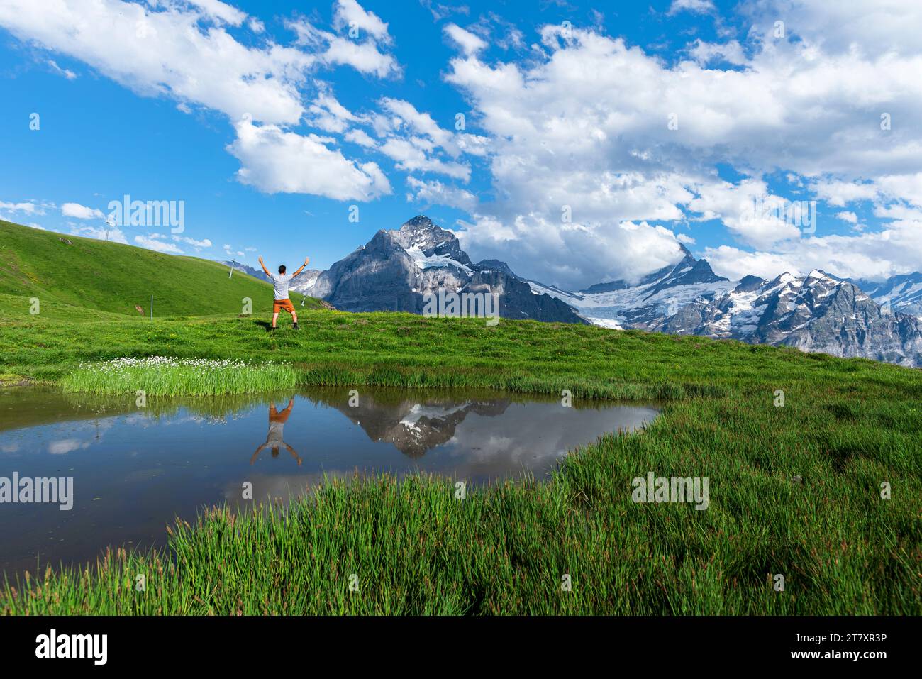 Felice escursionista che si riflette nelle acque di un piccolo lago sotto le montagne dell'Oberland Bernese, Bachalpsee, Grindelwald, Berna cantone, Svizzera, Europa Foto Stock