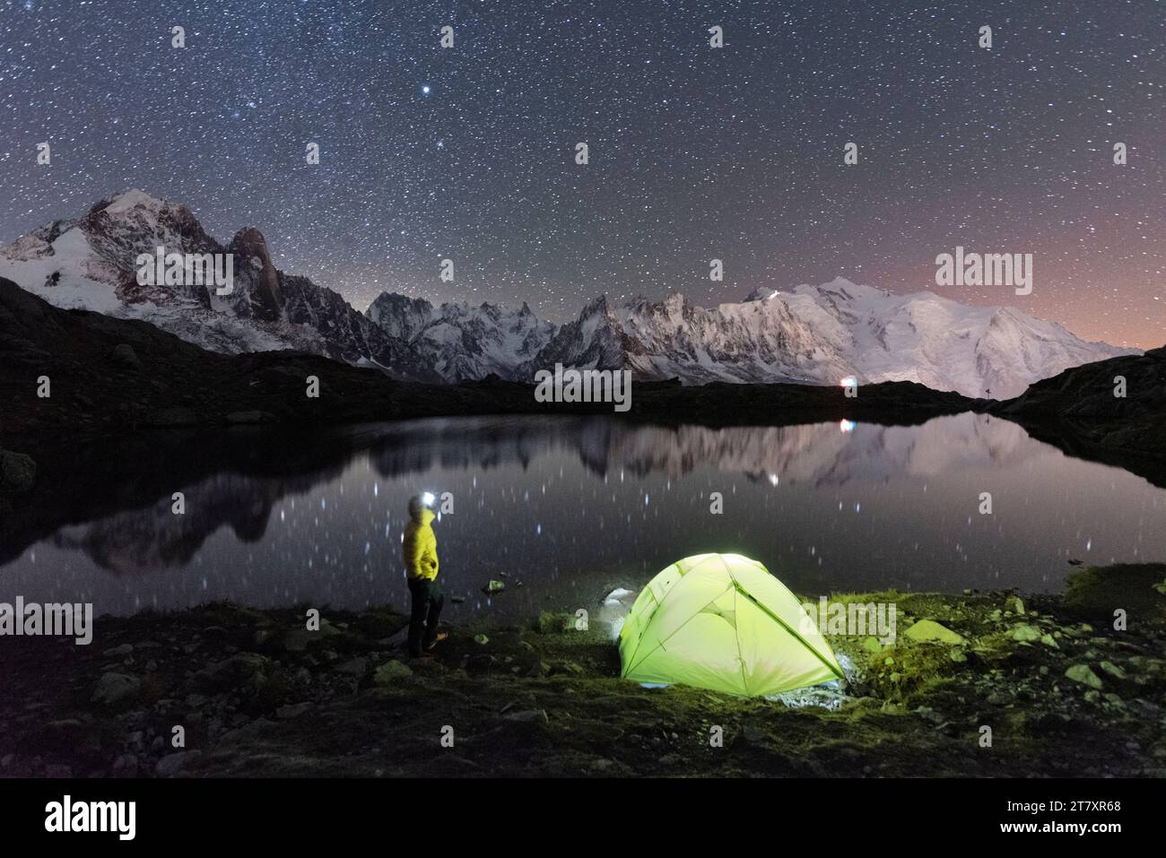 Persona che ammira il cielo stellato all'esterno della tenda che si trova sulla riva del lago Cheserys, circondato dal paesaggio alpino del Monte bianco Foto Stock